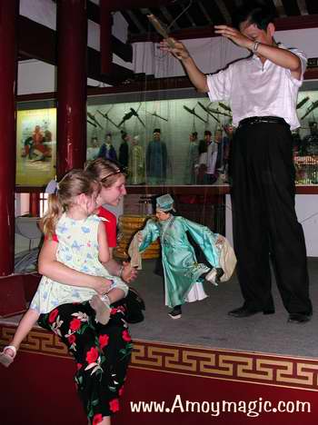 Quanzhou master puppeteer, Mr. Xia Rong Feng, entertains Ms. Jimmy Langley and her daughter Emma, at the Quanzhou Marionette Troupe museum and stage.